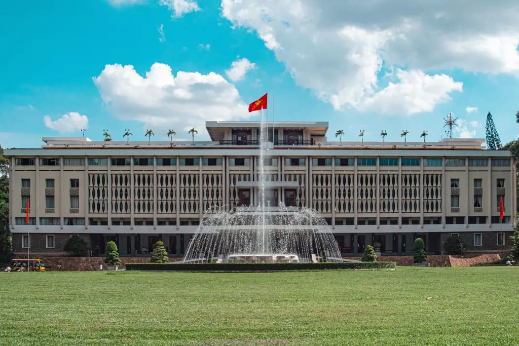 Front facade of the Independence Palace in Ho Chi Minh City with a water fountain spraying over a green lawn under a blue sky.